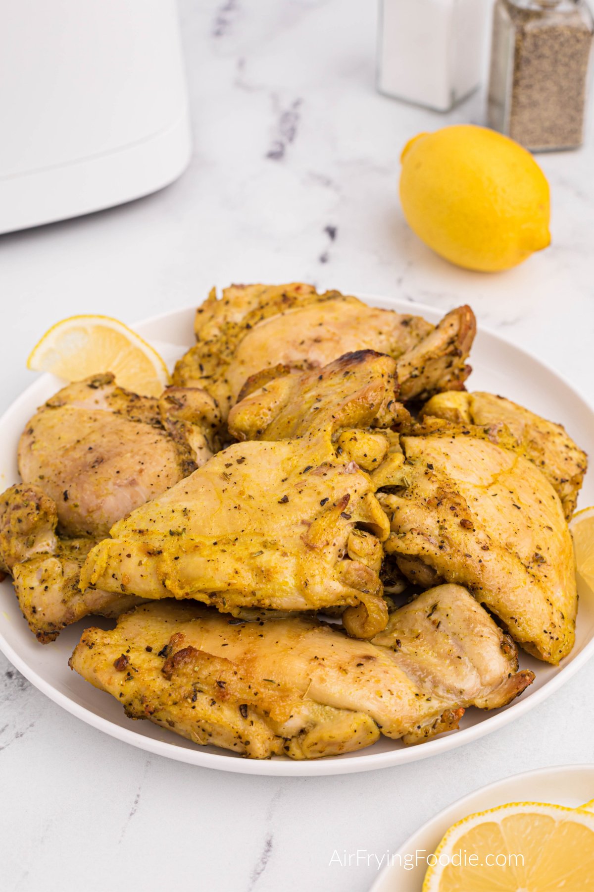 Plate full of lemon pepper chicken thighs made in the air fryer, served on a white plate with lemon wedges.