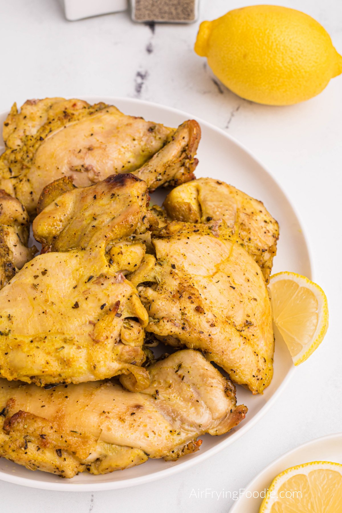 Close up of lemon pepper chicken thighs on a white plate with a lemon off to the side. 