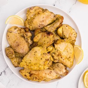 Air fried Lemon pepper chicken thighs on a white plate with lemon slices.