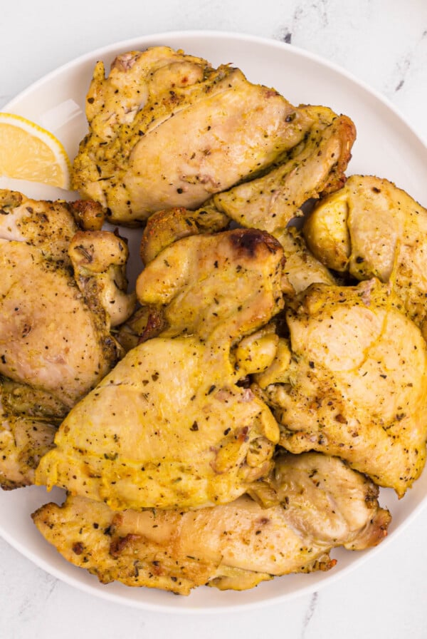 Air fried Lemon pepper chicken thighs on a white plate with lemon slices.