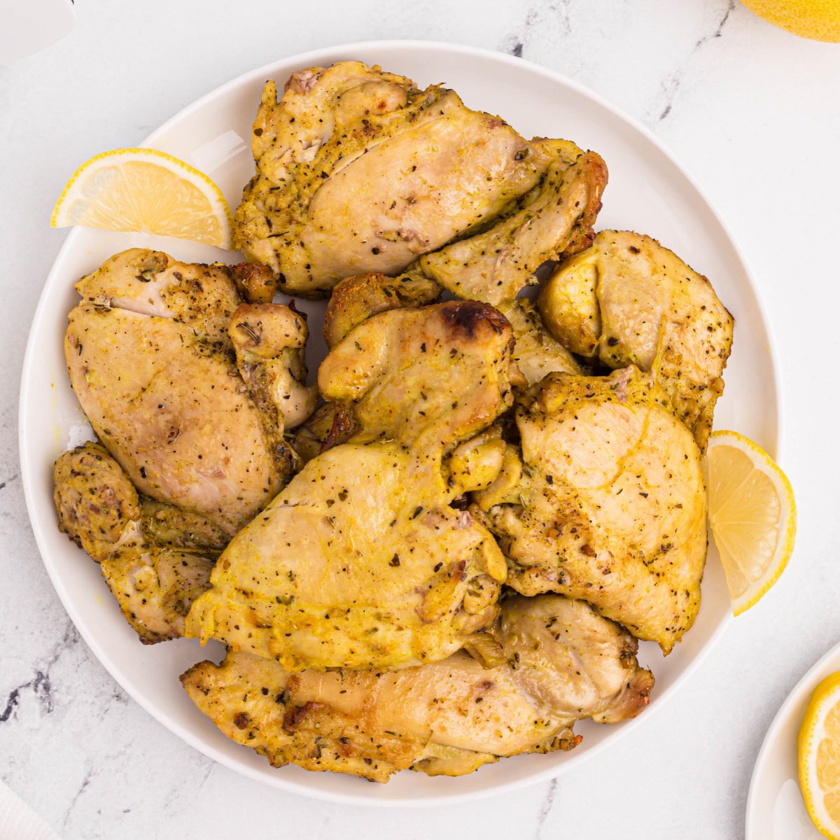 Air fried Lemon pepper chicken thighs on a white plate with lemon slices.