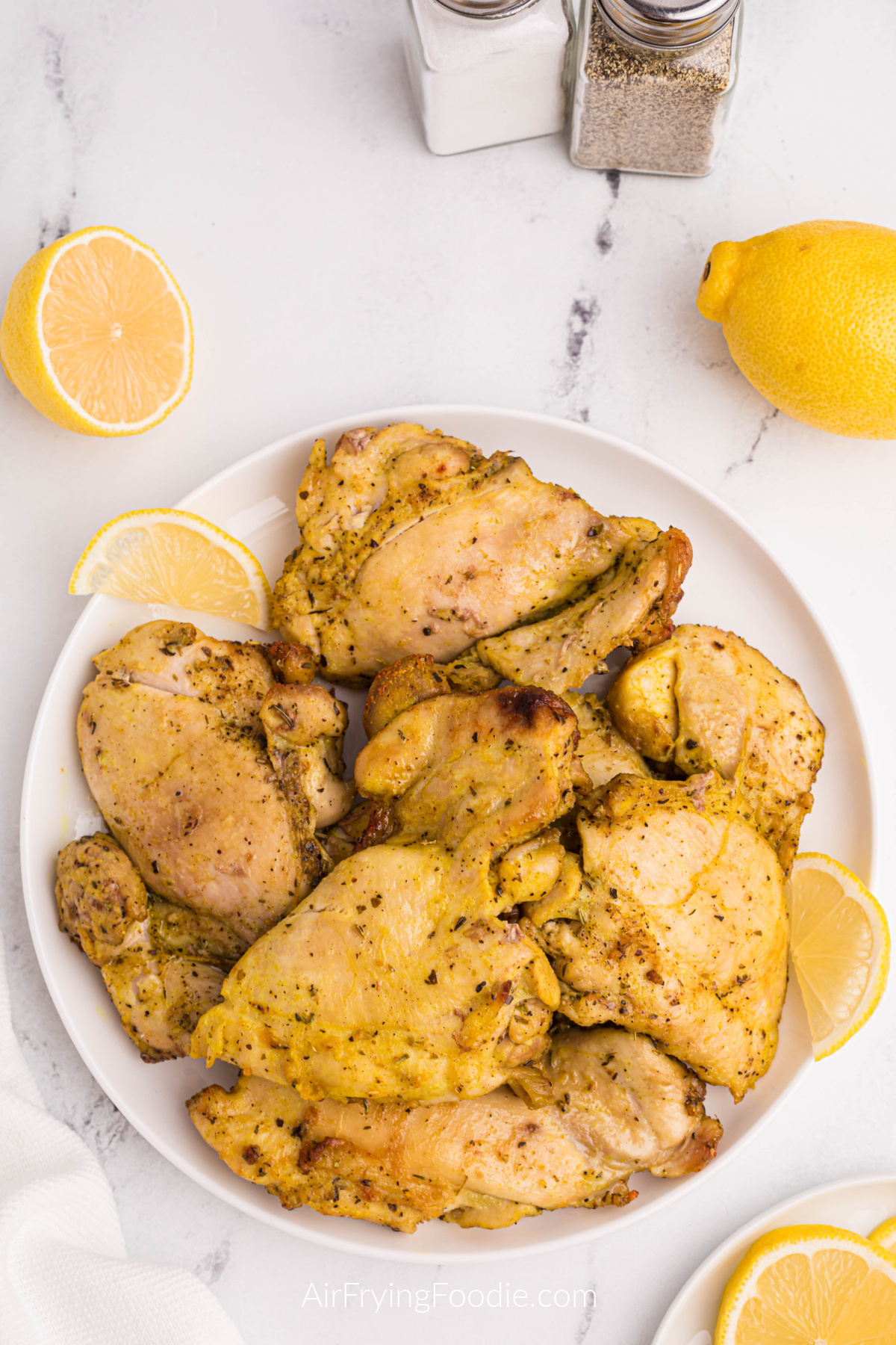 Lemon Pepper chicken thighs made in the air fryer, served on a white plate with lemon wedges. 