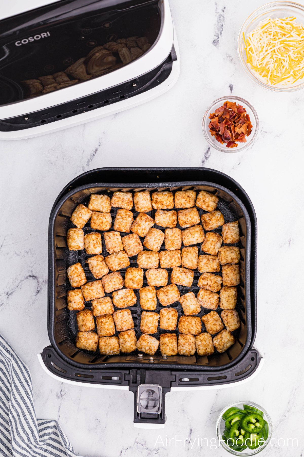 Frozen tater tots in the basket of the air fryer.
