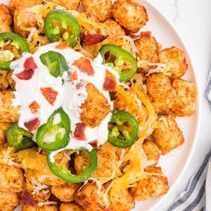 Loaded tater tots on a white plate with a dollop of sour cream, ready to serve.