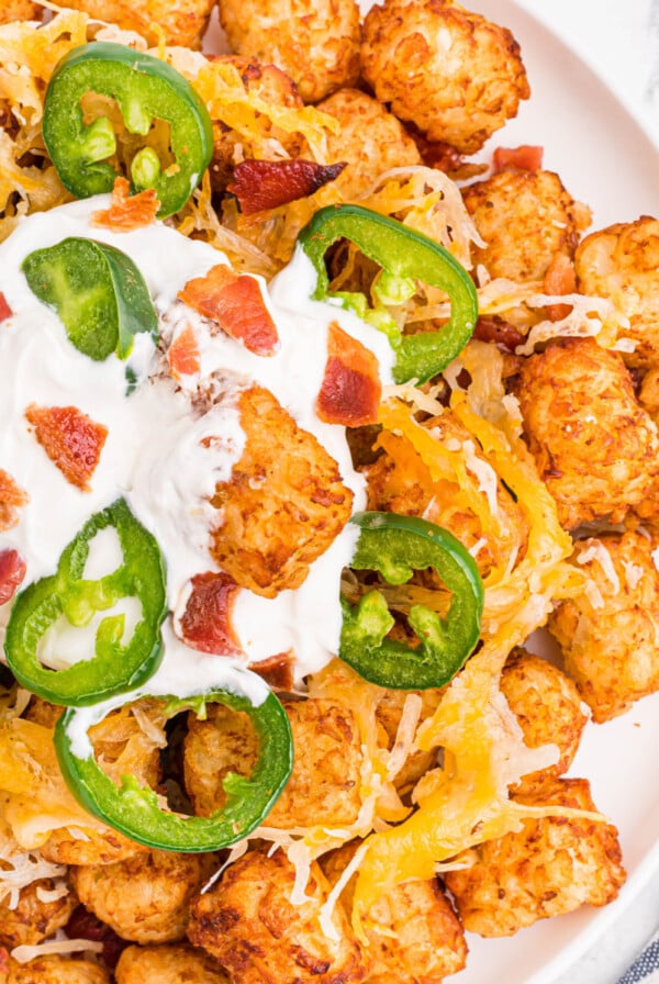 Loaded tater tots on a white plate with a dollop of sour cream, ready to serve.