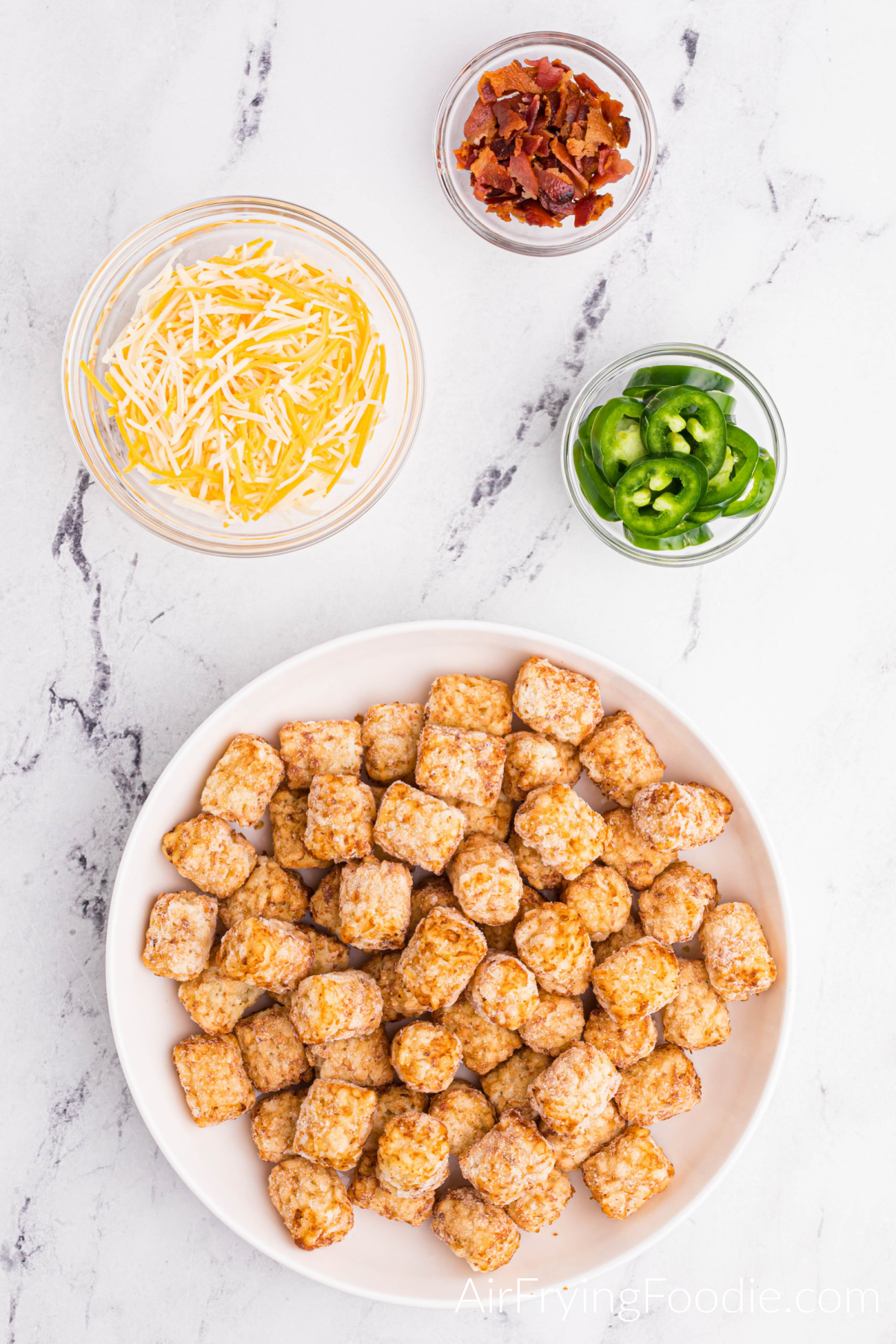 Plate full of frozen tater tots, and cheese, bacon, and jalapenos in bowls on a table.