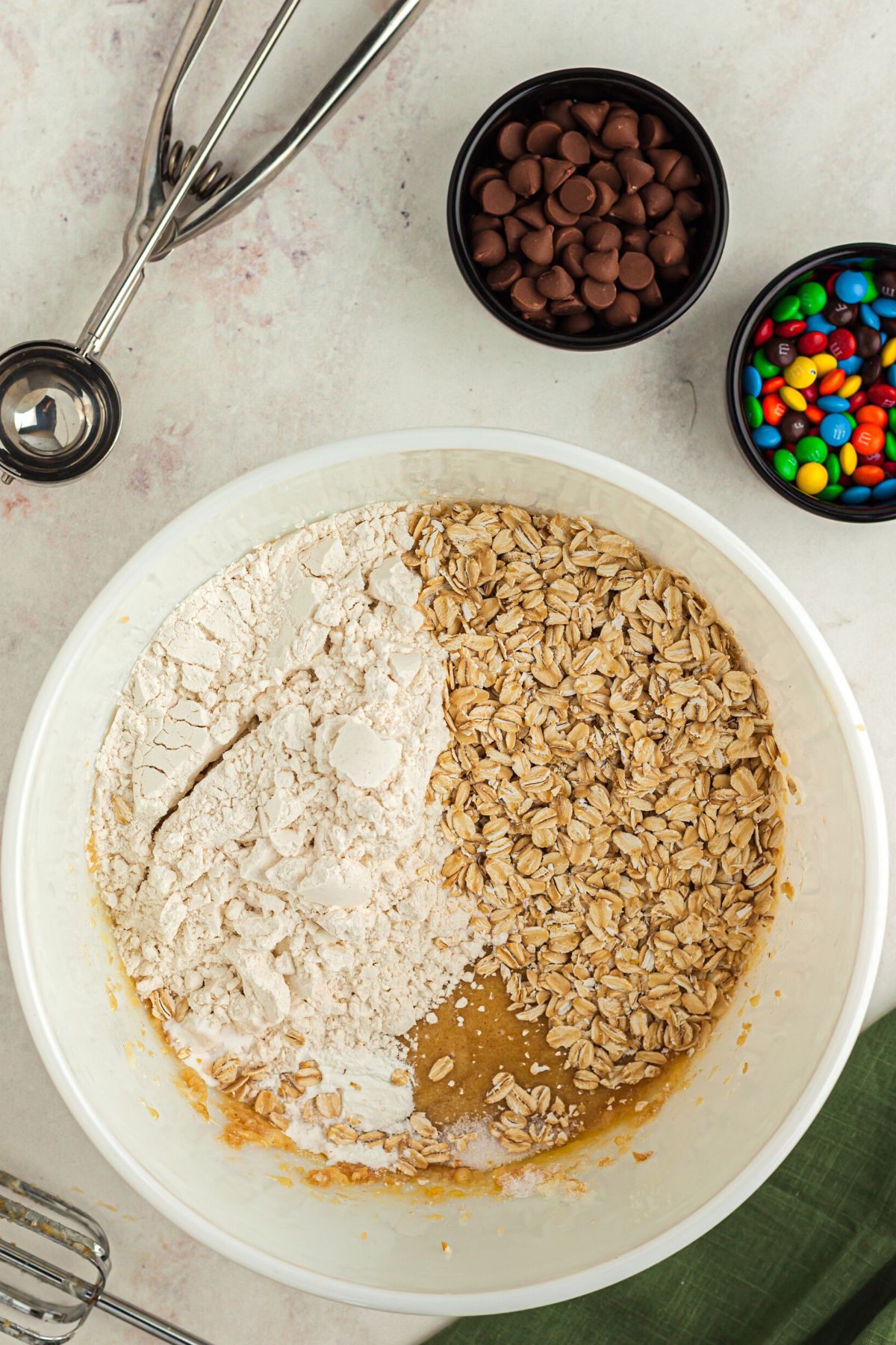 Oat and flour in a white mixing bowl with m and ms, chips on a marble table.