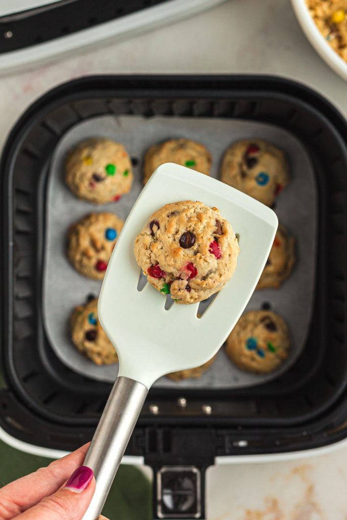 White spatula with monster cookie on it over the basket. 