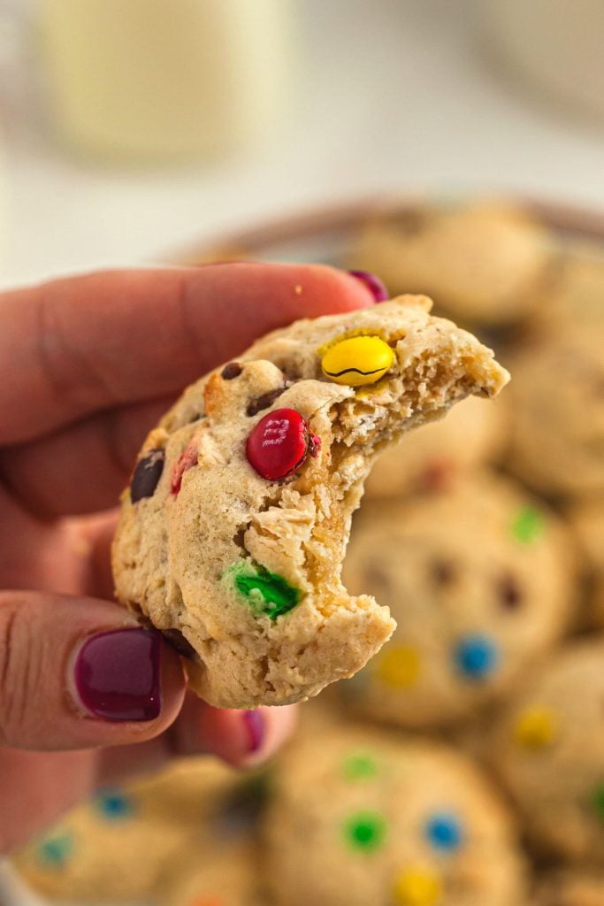 Cookie with bite being hold in hand showing m and ms.