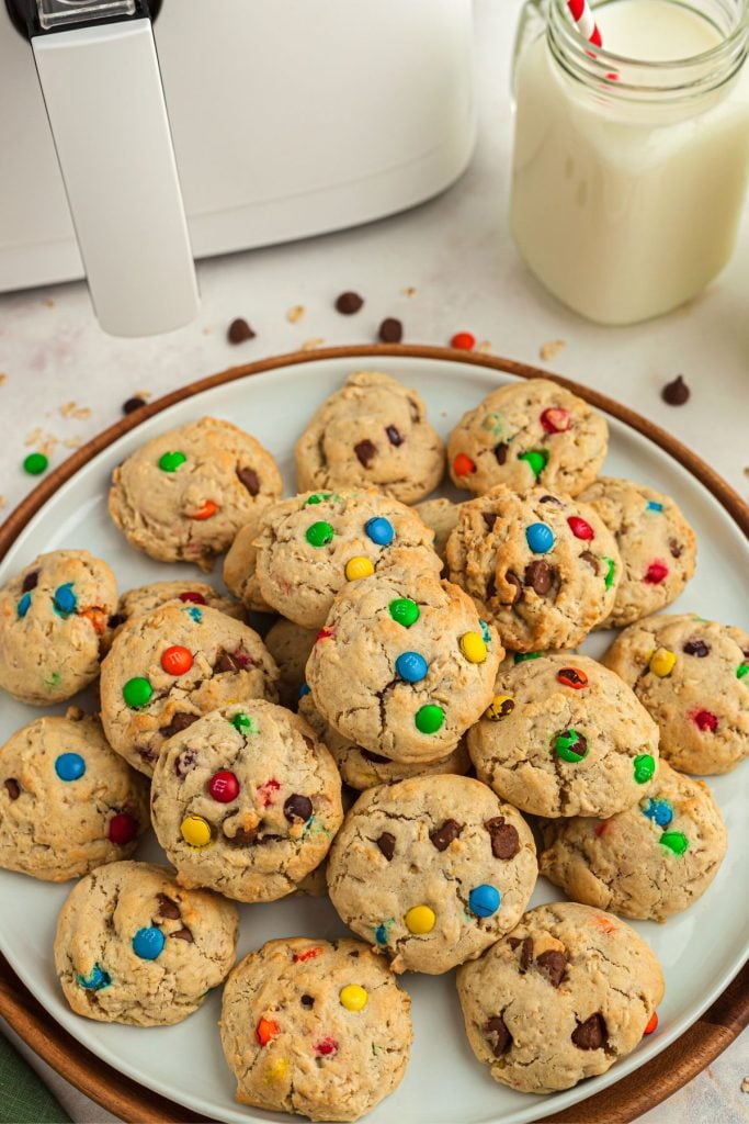 Large white plate with monster cookies stacked with m and ms and oats scattered on the table