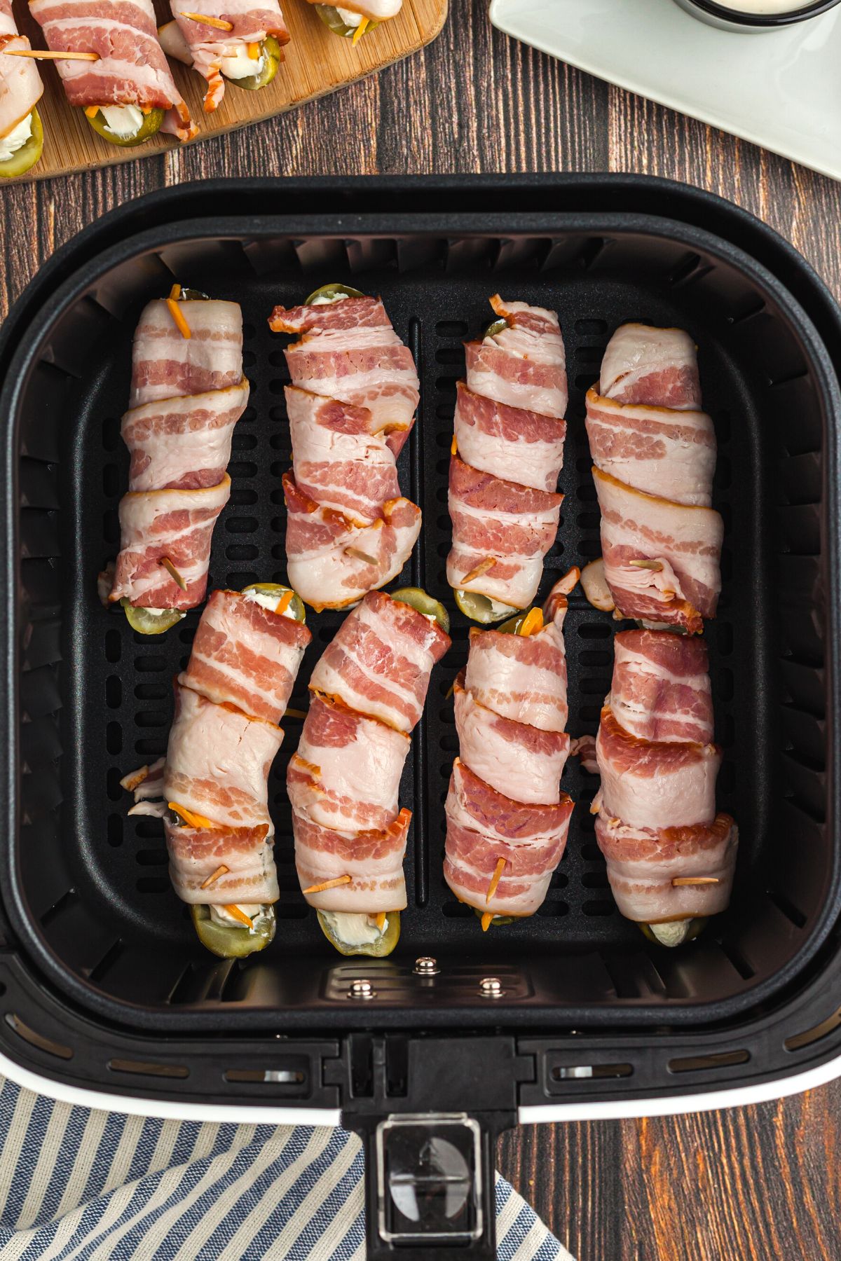 Bacon wrapped stuffed pickles in the air fryer basket before being cooked