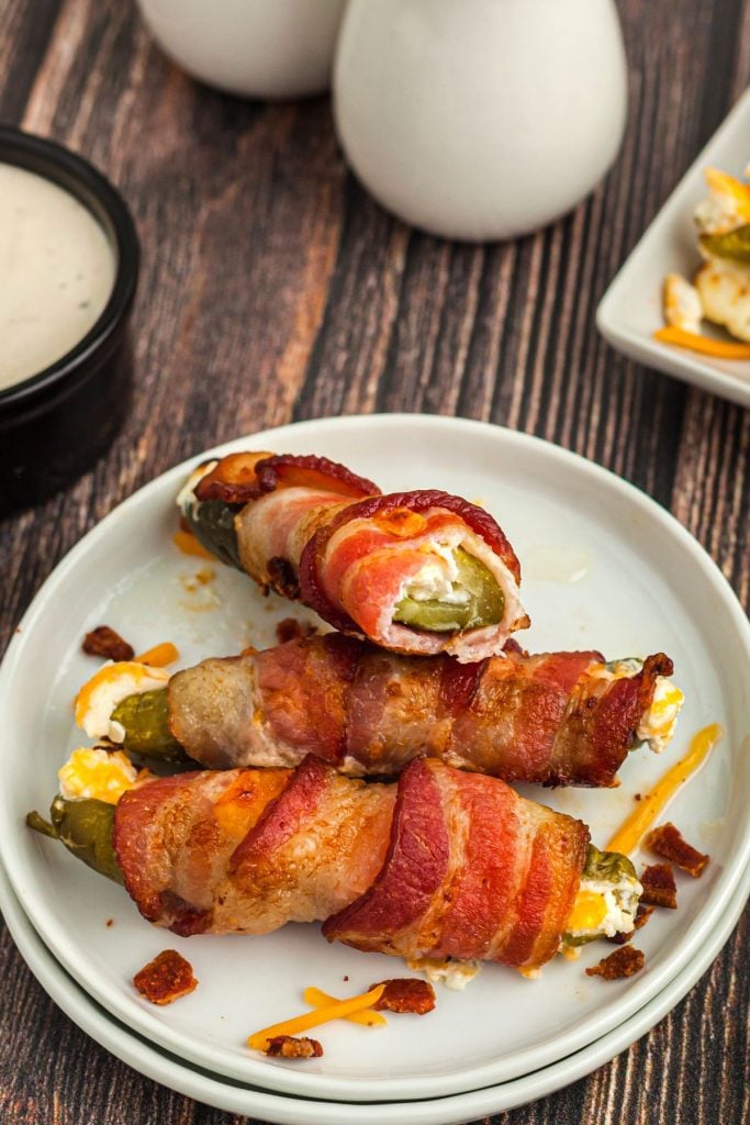 Stuffed pickle with cream cheese and wrapped in bacon on a small white plate.