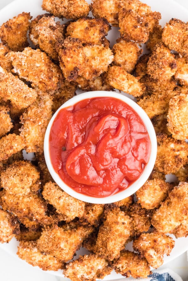 tray of popcorn chicken on a serving plate with a bowl of ketchup for dipping.