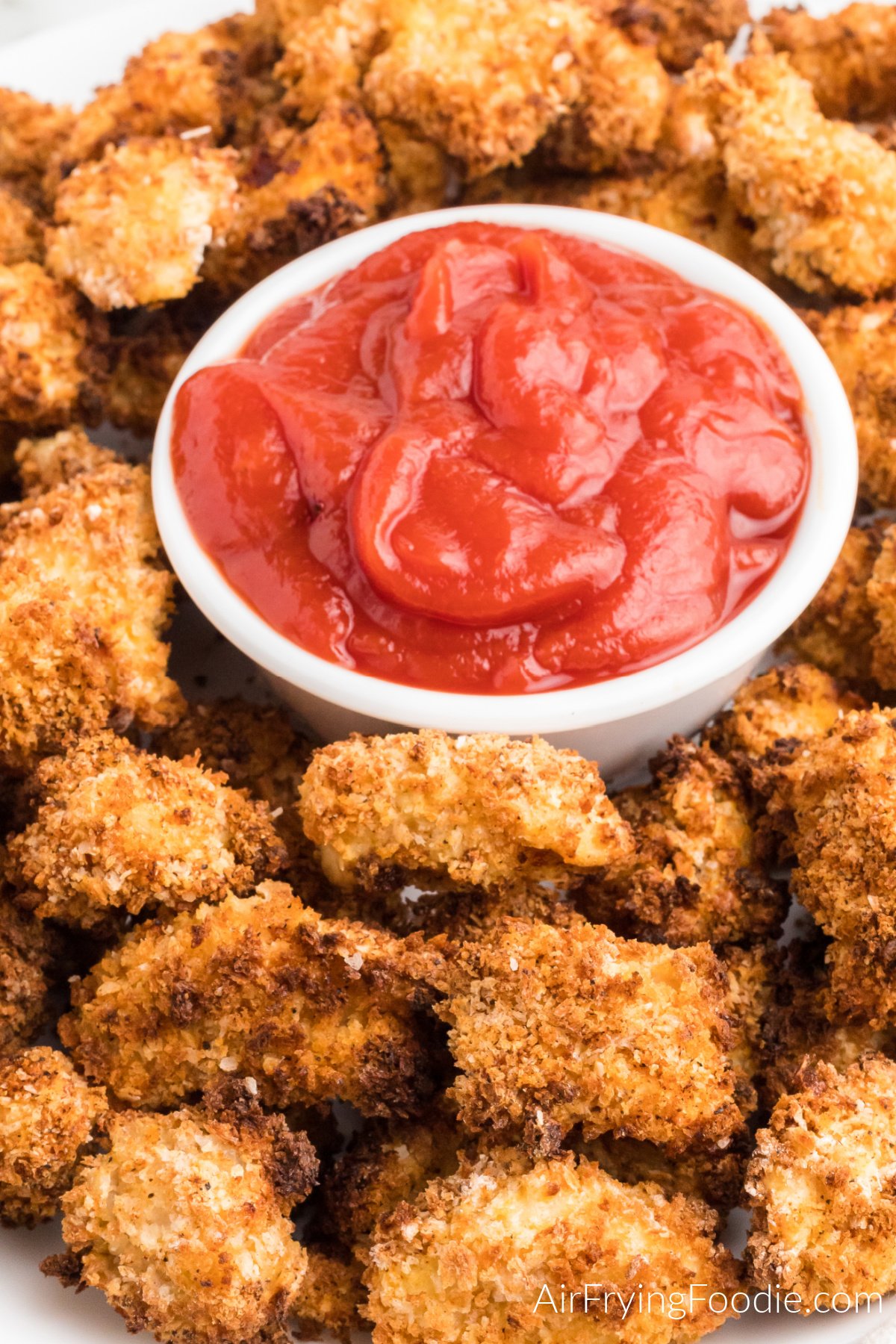 Homemade popcorn chicken made in the air fryer, on a serving tray with a side of ketchup.