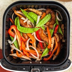 Juicy chicken and stir fry veggies in a an air fryer basket after being cooked
