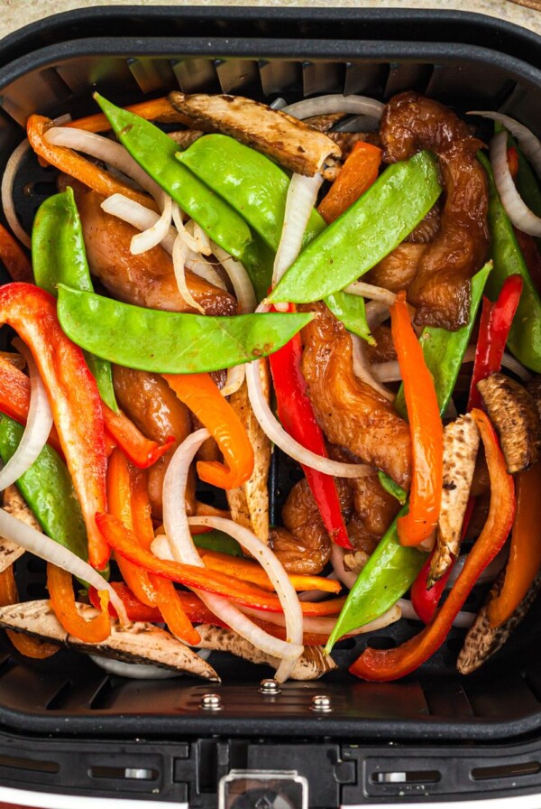 Juicy chicken and stir fry veggies in a an air fryer basket after being cooked