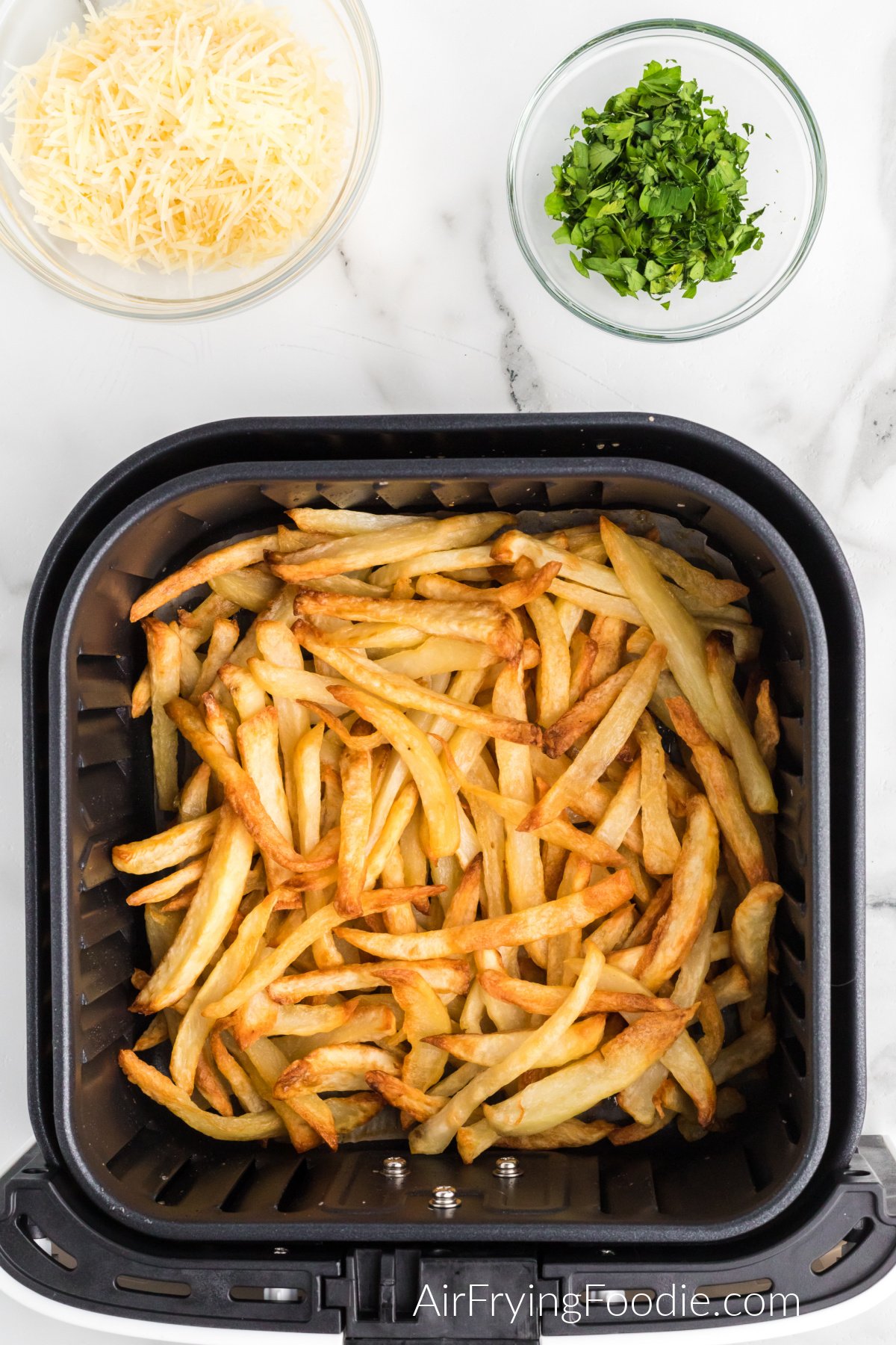 Truffle fries in the basket of the air fryer ready to be tossed with cheese and parsley.