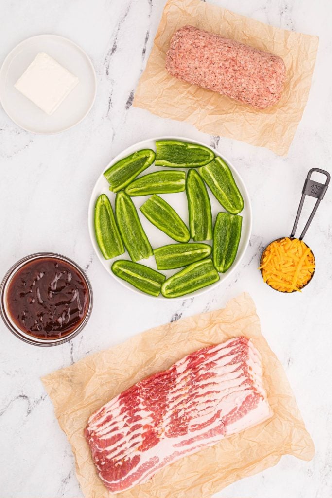 Ingredients needed to make jalapeno wrapped with sausage and bacon on a white marble table. 