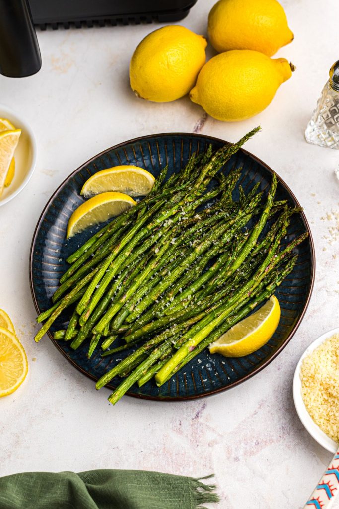 Green asparagus on a dark blue plate sprinkled with asparagus and served with lemon wedges