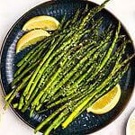 Green juicy asparagus on a black plate with lemon wedges.