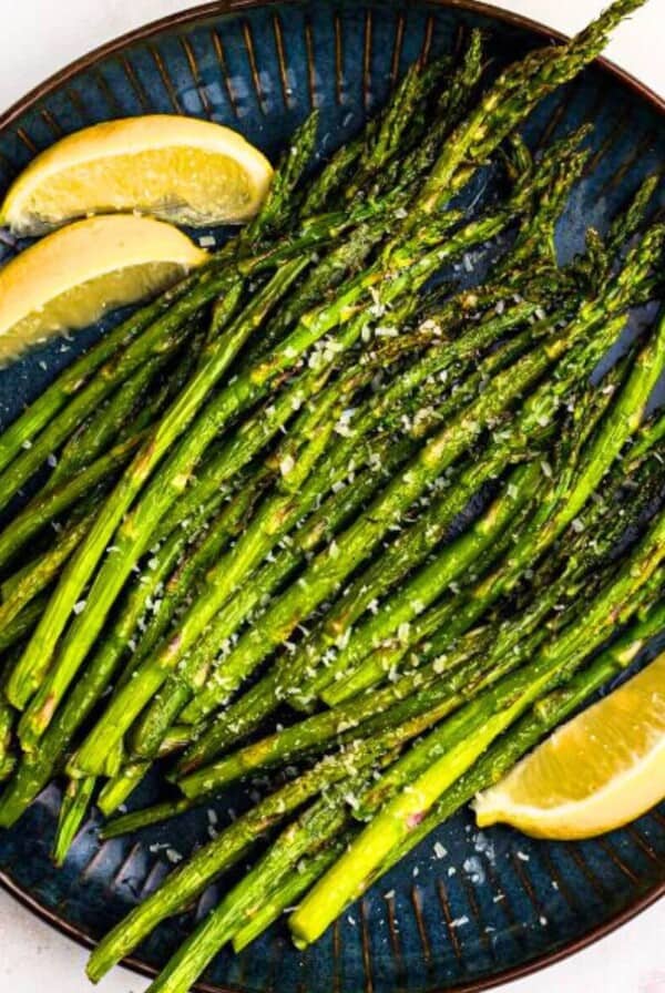 Green juicy asparagus on a black plate with lemon wedges.