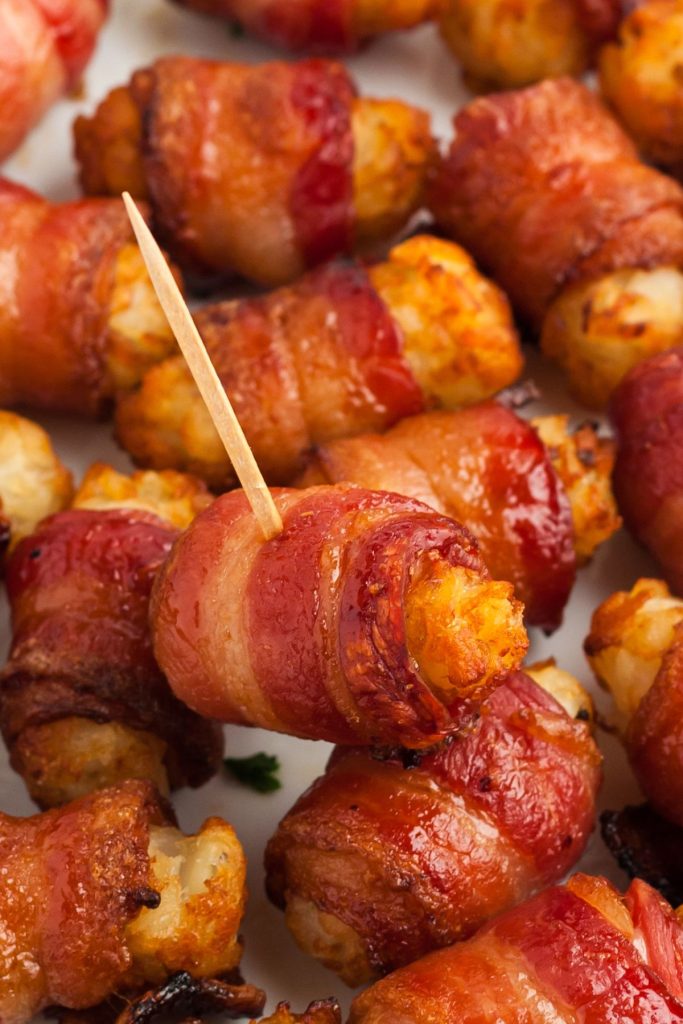 Juicy crispy bacon wrapped tater tots stacked on a white plate