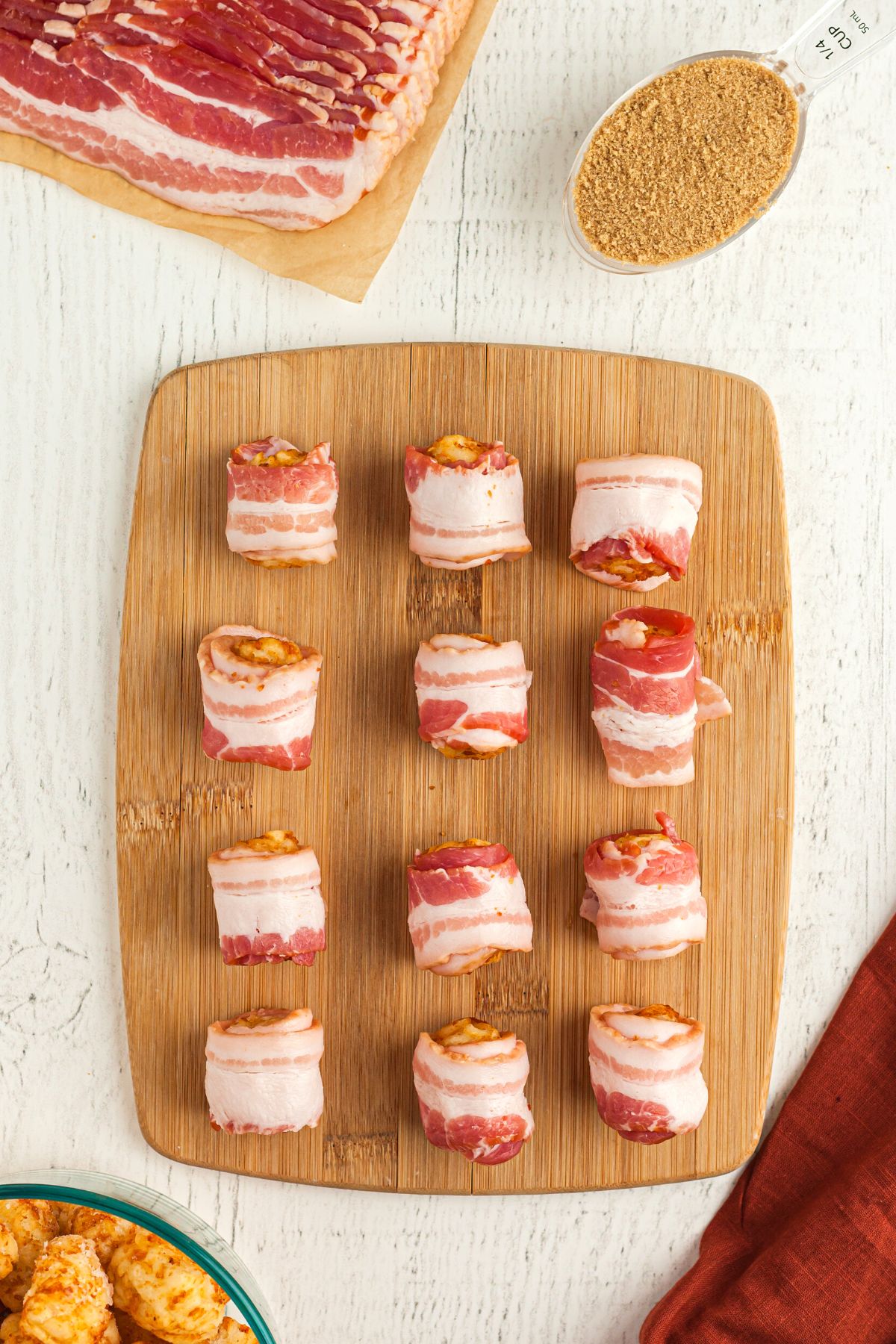 Tater tots wrapped in slices of bacon on a wooden cutting board
