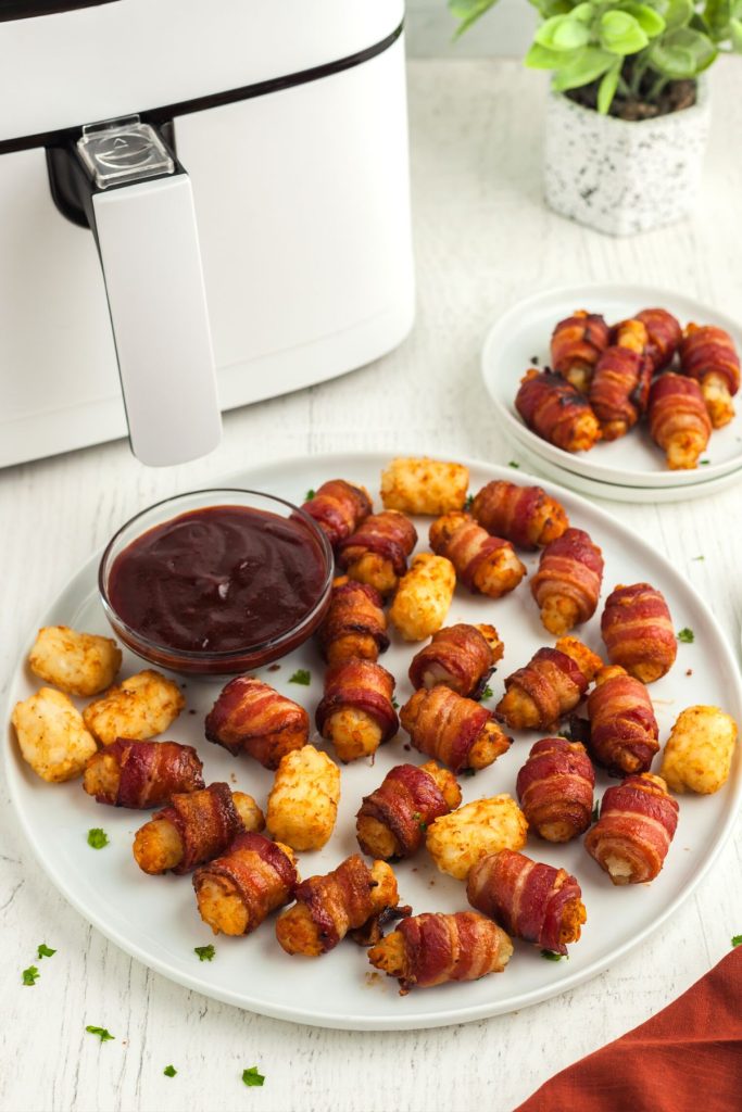 Golden bacon wrapped tater tots on a large white plate with BBQ sauce 