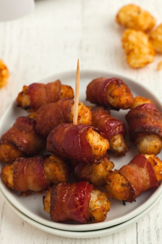 Small white plate with golden crispy bacon wrapped tater tots