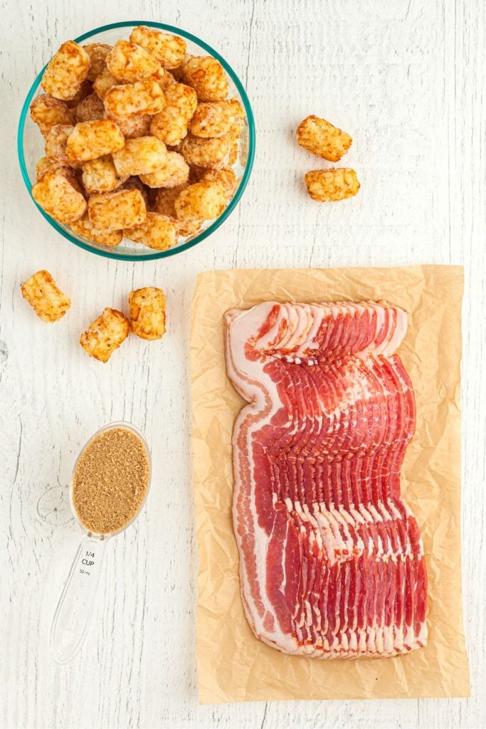 Ingredients needed to make bacon wrapped tater tots on a white wooden board