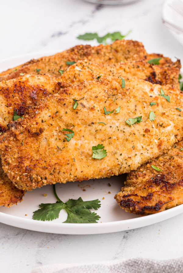 Fully cooked in the air fryer, chicken cutlets served on a white plate with parsley.