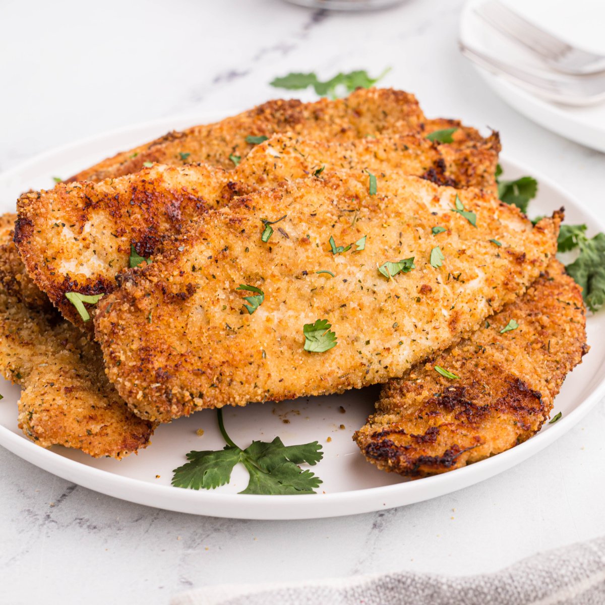 Fully cooked in the air fryer, chicken cutlets served on a white plate with parsley.