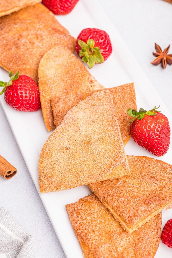 Golden cinnamon and sugar coated tortilla chips on a white plate with fresh strawberries