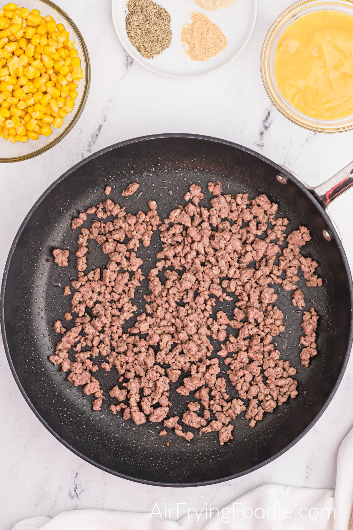 Ground beef cooked in a skillet with two clear bowls, one with corn and the second bowl with cream of soup, and the round plate showing the spices.
