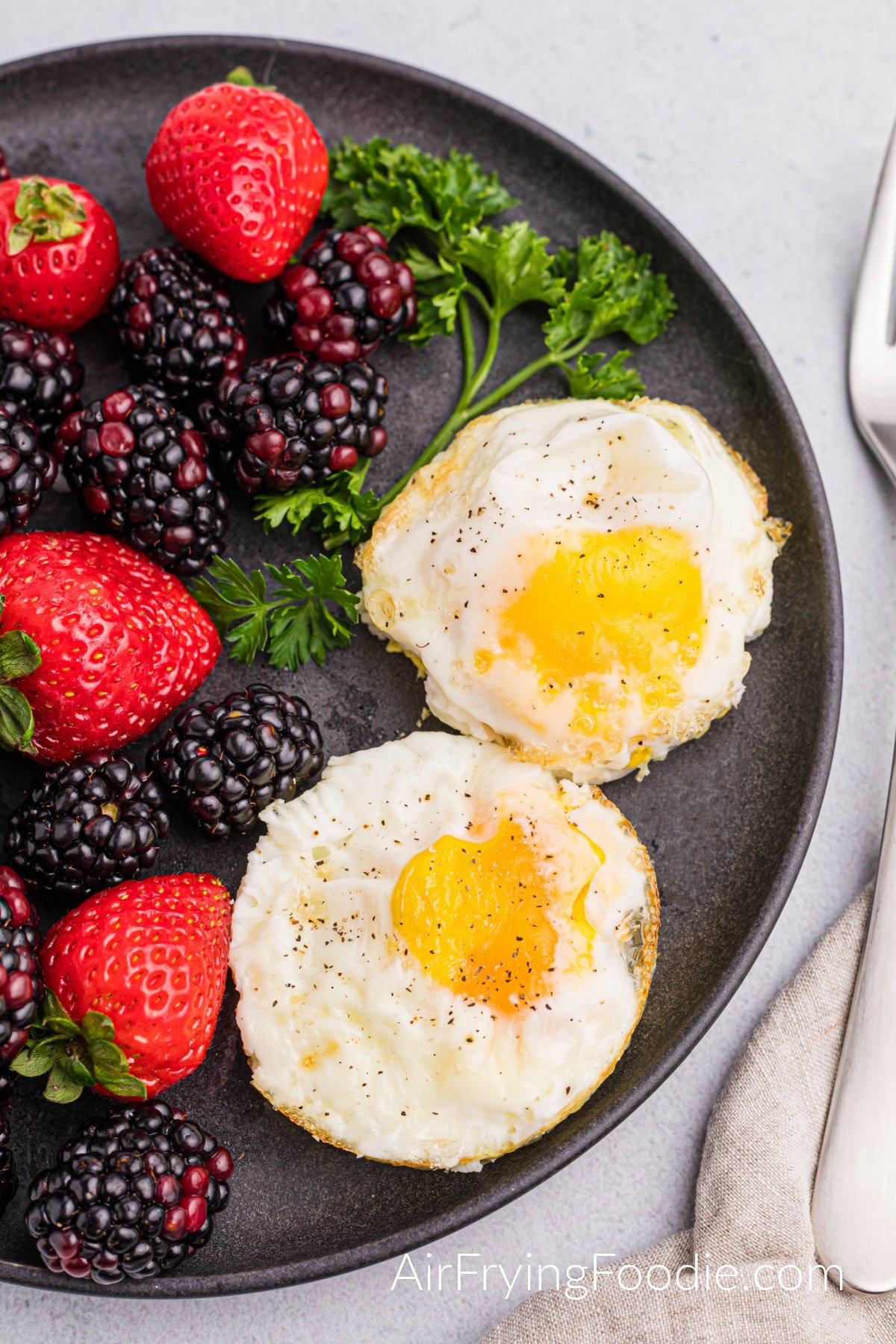 Air Fried eggs with salt and pepper and a side of fruit on a plate.
