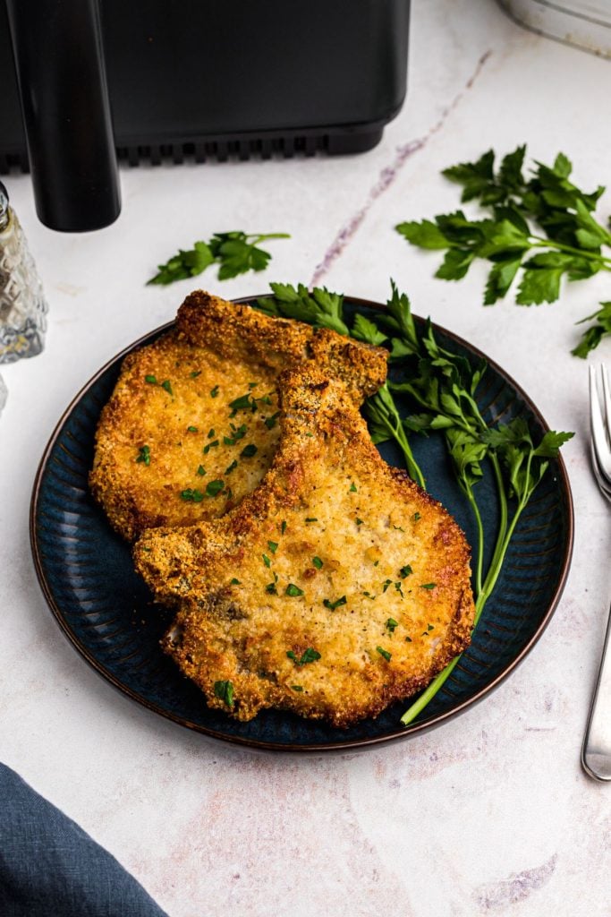 Lightly breaded pork chops on a blue plate garnished with parsley
