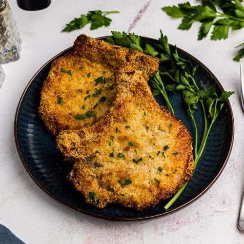 Golden coated gluten free pork chops on a blue plate and garnished with parsley