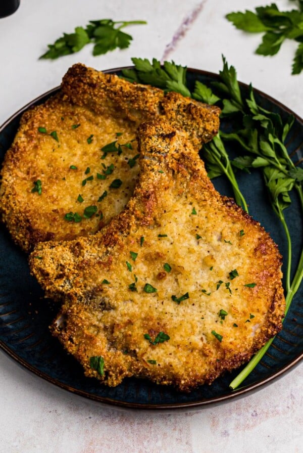 Golden coated gluten free pork chops on a blue plate and garnished with parsley