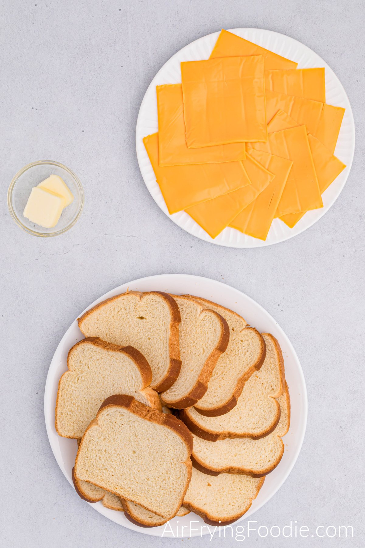 Bread overlapping in a circle on a round white plate. American cheese covering the bottom of a round white plate and a ramekin on butter. 
