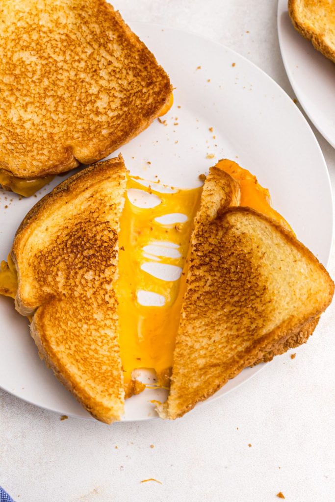 golden crispy grilled cheese sandwich sliced with melty cheese coming out. 