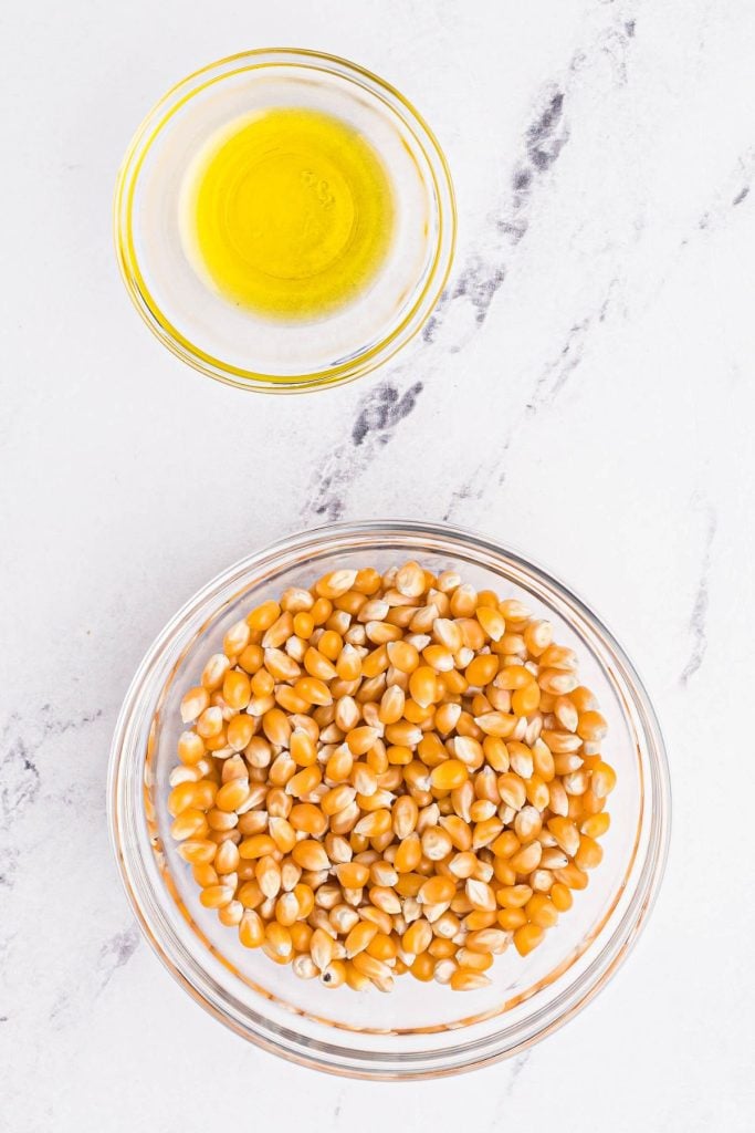 Popcorn kernels and melted butter in glass bowls on a marble table. 