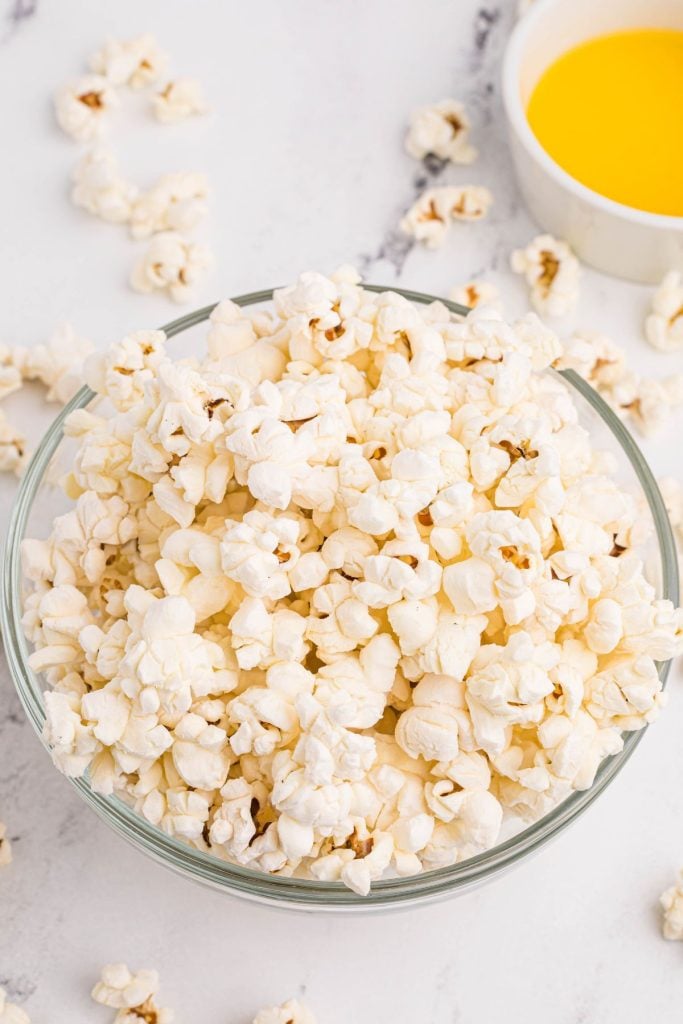 White fluffy popcorn in a clear glass bowl with melted butter in a small side dish.