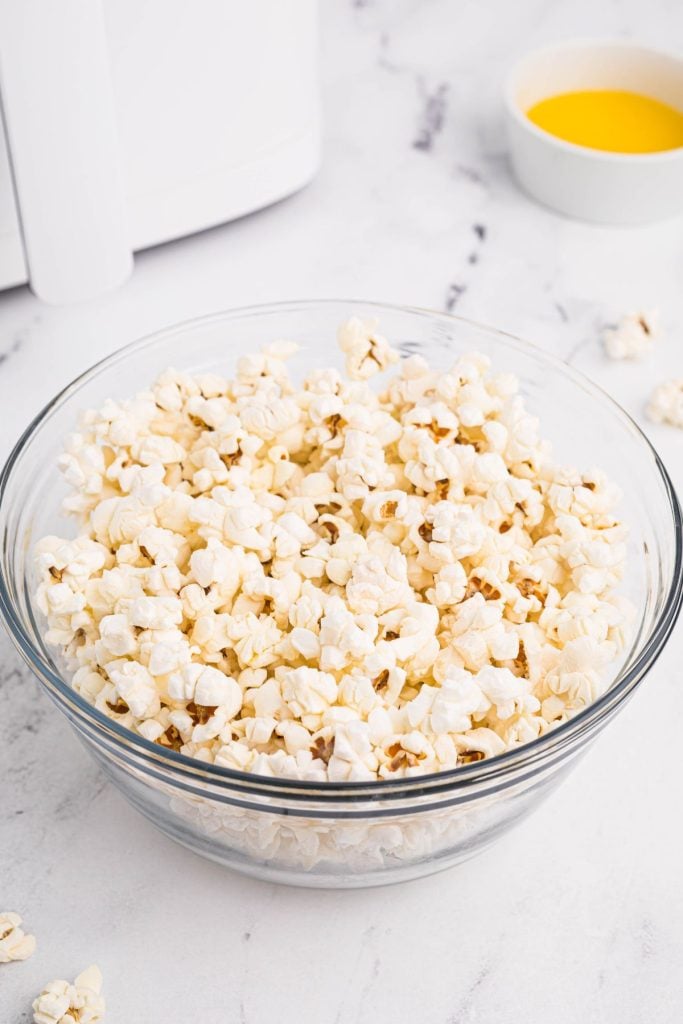 White fluffy popcorn in a clear glass bowl with melted butter in a small bowl