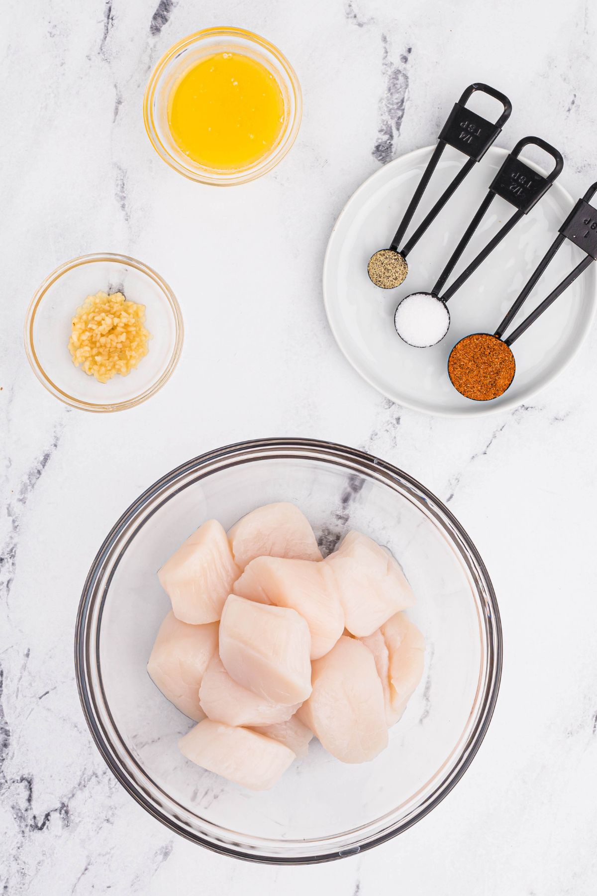 Ingredients of scallops, garlic, and seasonings on a white marble table