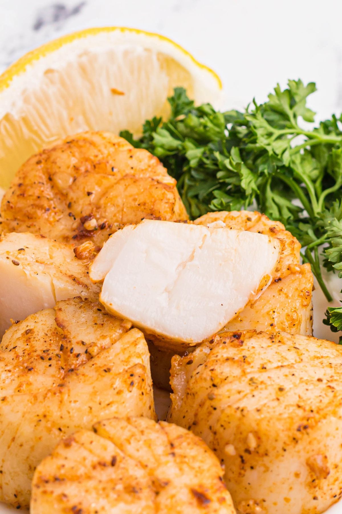 Golden juicy scallops stacked on a plate with parsley garnish