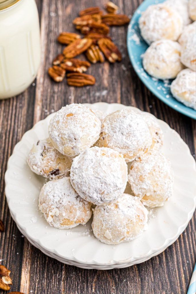 White plate with stacked powdered sugar coated snowball cookies on a wooden table