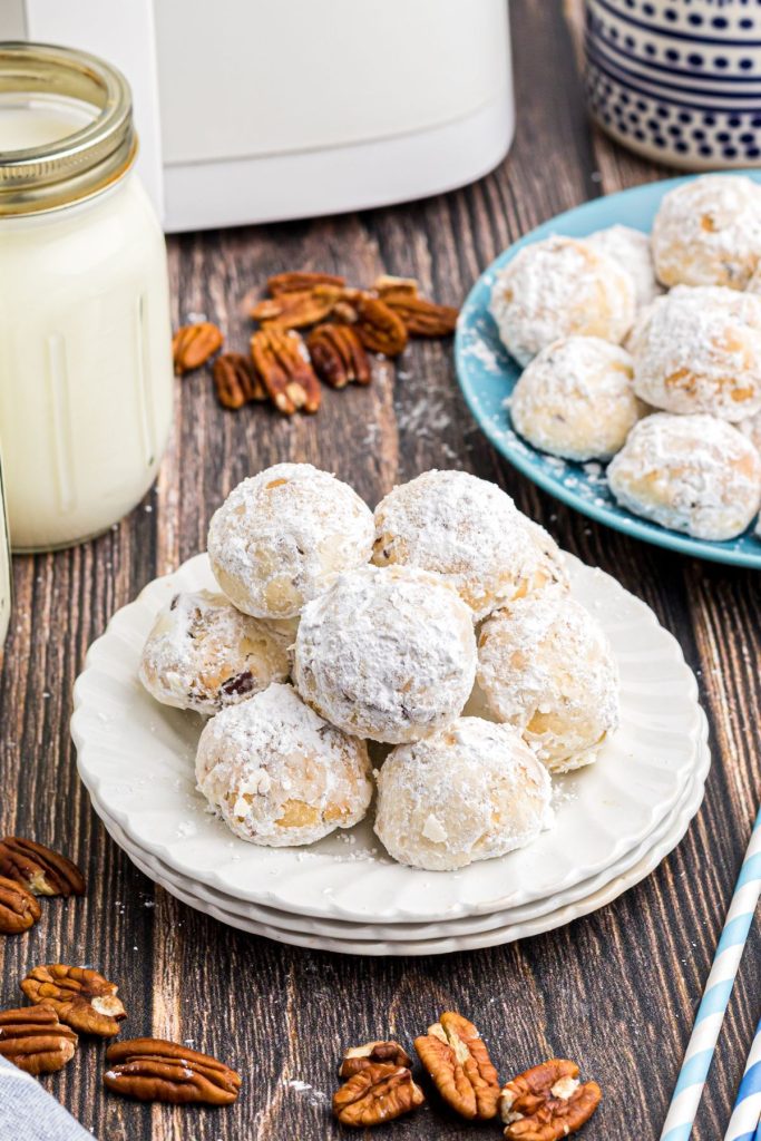 White powdered sugar coated cookies on a white plate in front of the air fryer