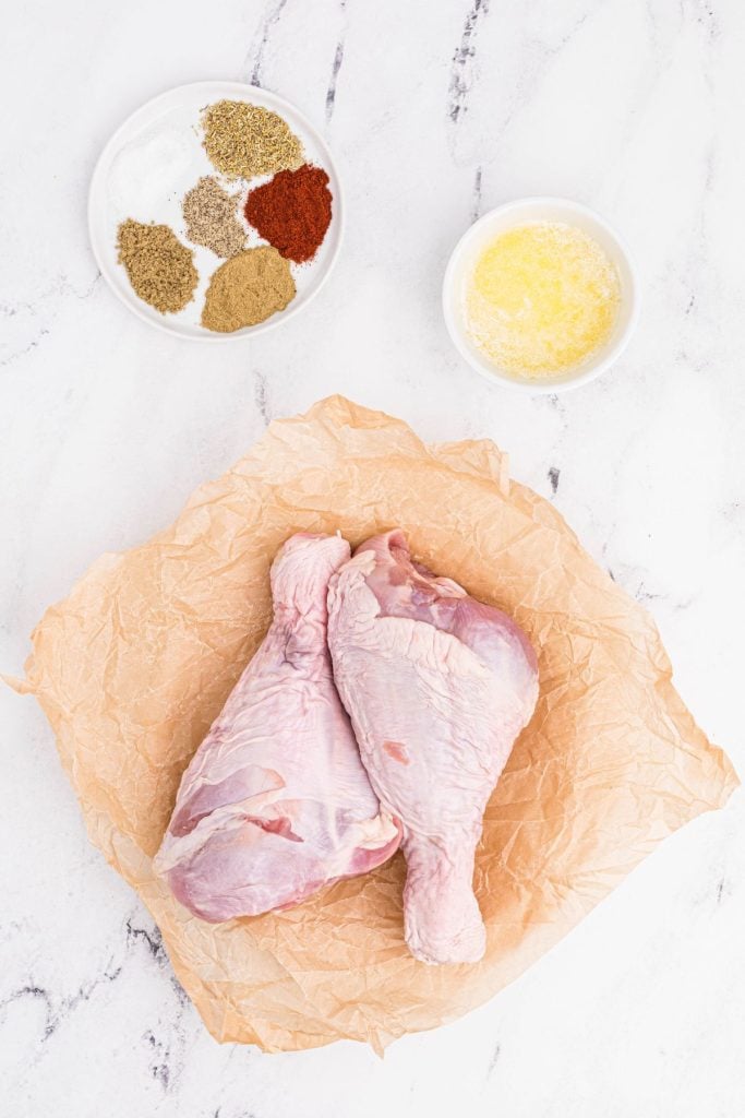 Ingredients measured out and on a white marble table including uncooked turkey drumsticks