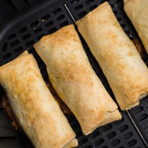 Air fried burritos in the basket of the air fryer.