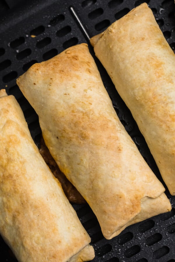 Air fried burritos in the basket of the air fryer.